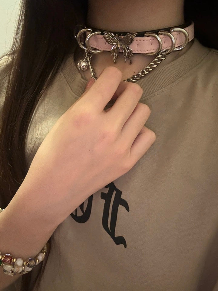 Worn photo of the black and pink butterfly choker, showing the chunky silver chain, dainty bell and ornate butterfly charm. Styled with a graphic t-shirt and gold charm bracelets.