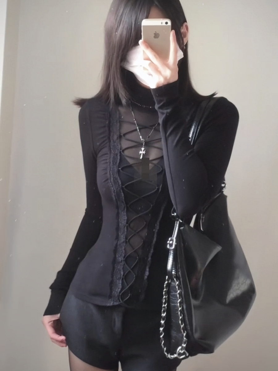 Modelled photo of a black lace-up top with turtleneck collar, sheer central bodice panel, long sleeves and elastic corset lacing. Styled with a silver cross necklace, black handbag and black shorts.