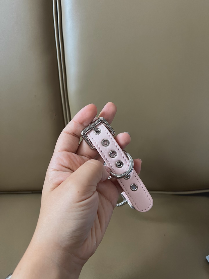 Rear view of a pink and holographic silver leather choker showing the adjustable stainless steel plated buckle and sizing holes for a versatile fit. Held by a hand against a beige sofa for a casual lifestyle shot.