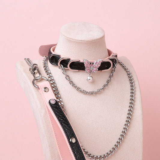 Black and pink leather choker and leash set featuring a silver and pink diamante butterfly charm, silver chains, D rings and bell, with detachable chain leash and leather hand strap. Displayed on a white mannequin bust against a pink background for a pastel goth aesthetic.