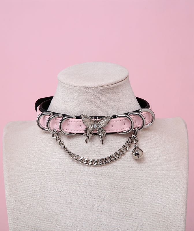 Black and pink leather choker featuring a stainless steel plated butterfly charm, D rings, chain and bell. Displayed on a white mannequin bust against a pink background for a pastel goth aesthetic.