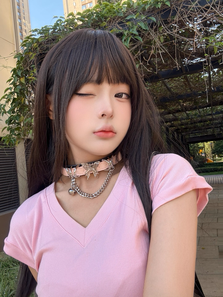 Worn photo of a black and pink leather choker featuring a stainless steel plated butterfly charm, D rings, chain and bell. Styled with long brown hair and pink t-shirt for a casual kawaii look.