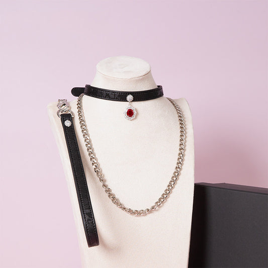Black leather choker and leash set featuring clear and red crystal cameo and hardware, detachable silver chain leash and black leather hand strap. Displayed on a white mannequin bust against a pink background for a pastel goth aesthetic.