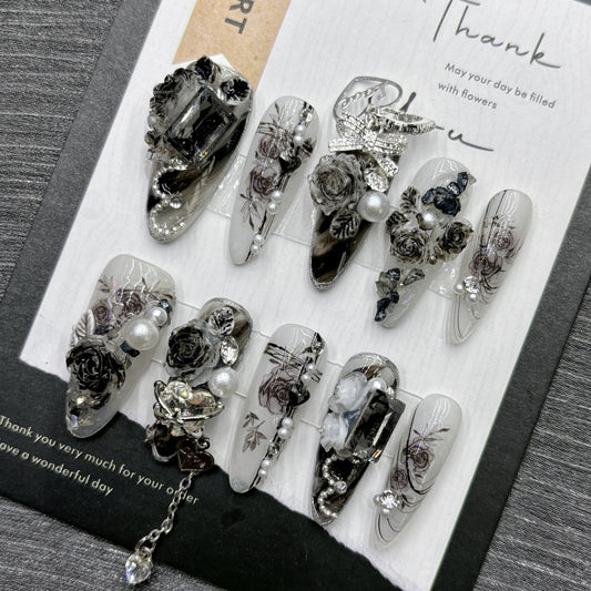 Black and white long stiletto false nails featuring a gothic rose pattern, silver and diamante bow and heart charms, white pearl beads and clear diamantes, displayed on a black and white display card.