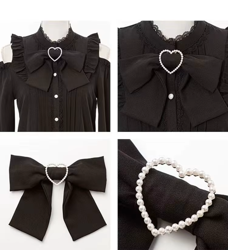 Detail photo of a black polyester blouse featuring lace trimmed collar, detachable black ribbon bow with a white pearl heart centrepiece, white pearlescent buttons and cold shoulder cut-outs, displayed on a white background.