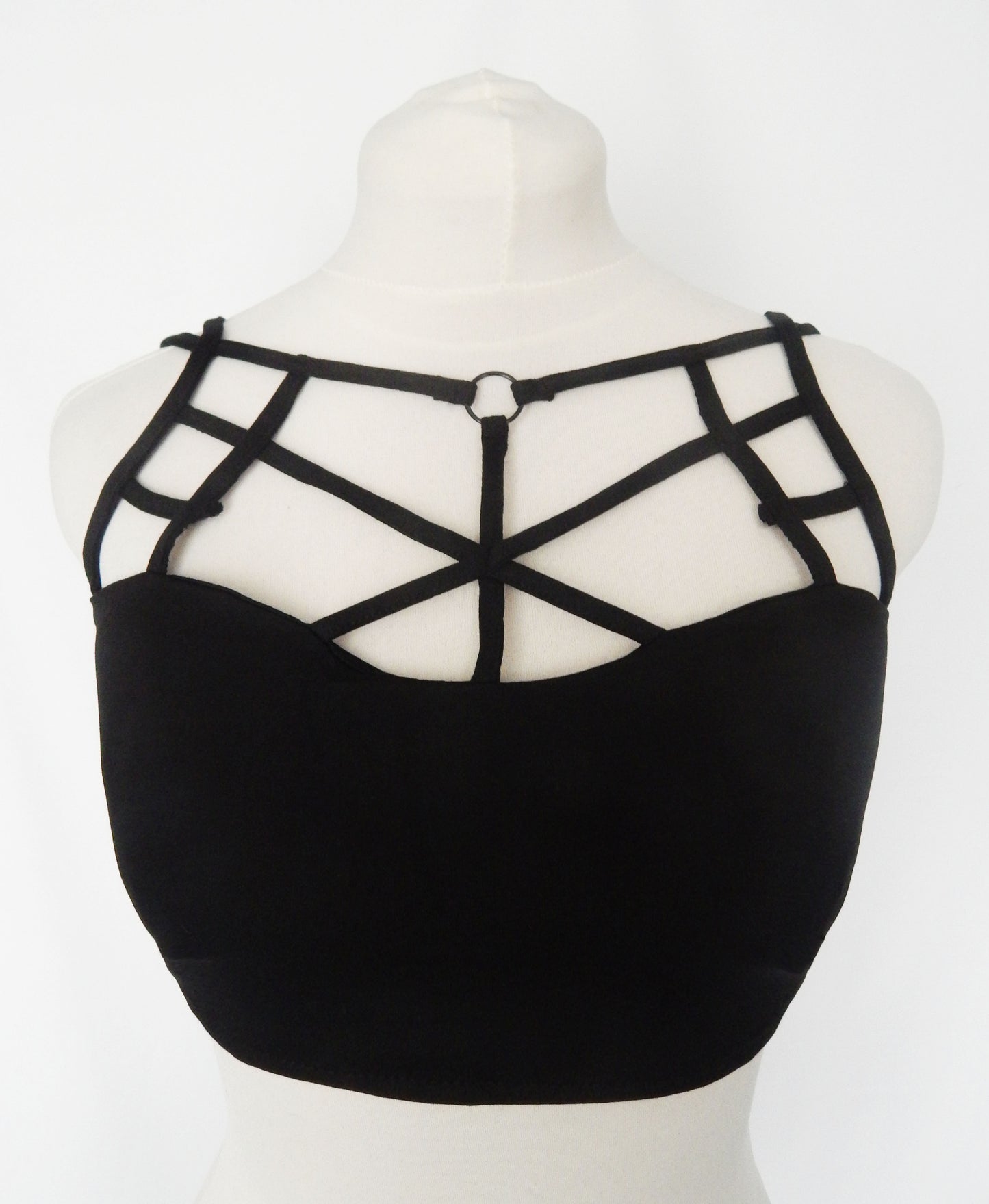 Black strappy crop top with a structured sweetheart neckline and geometric cage-style straps on a white mannequin torso.