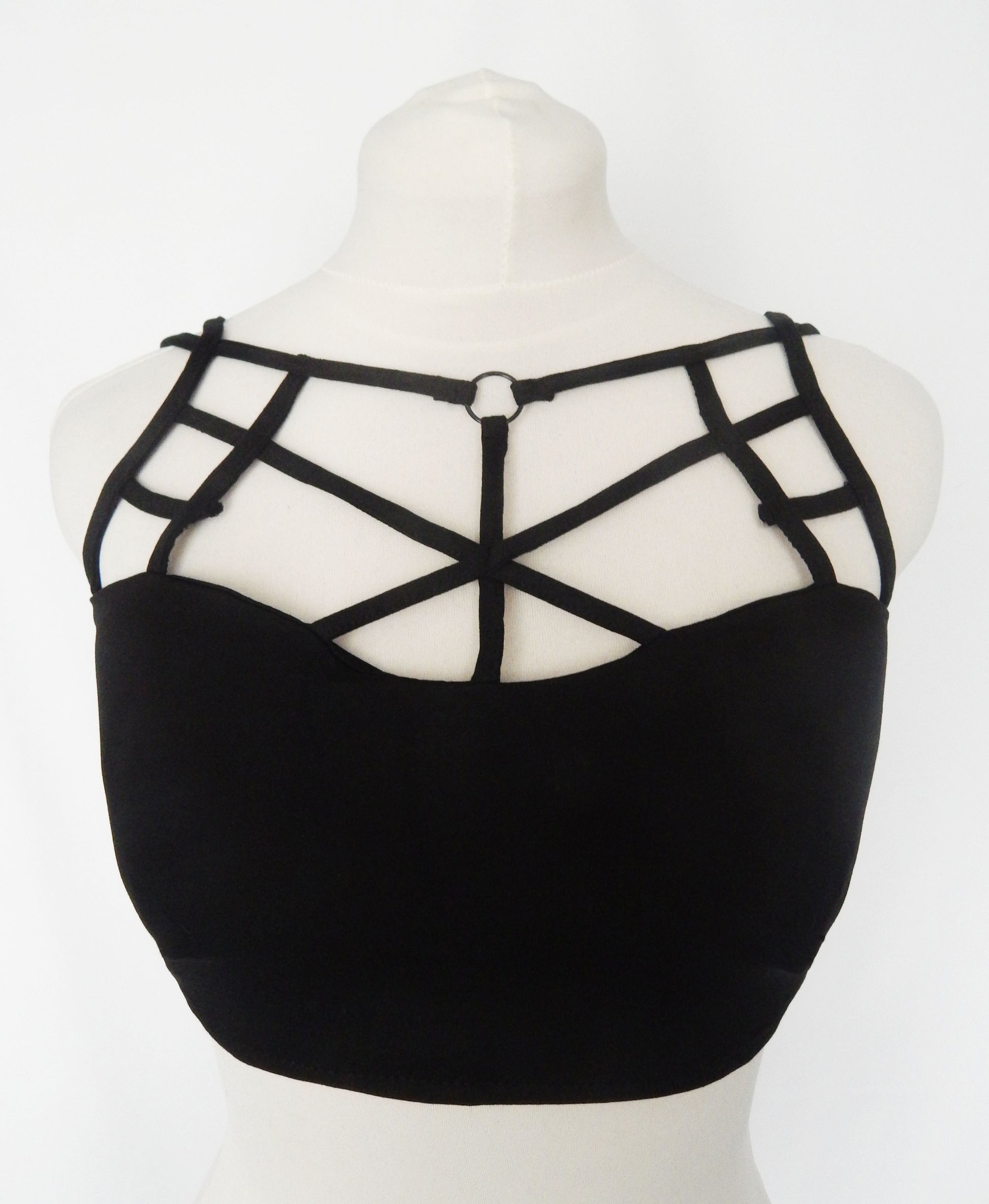 Black strappy crop top with a structured sweetheart neckline and geometric cage-style straps on a white mannequin torso.