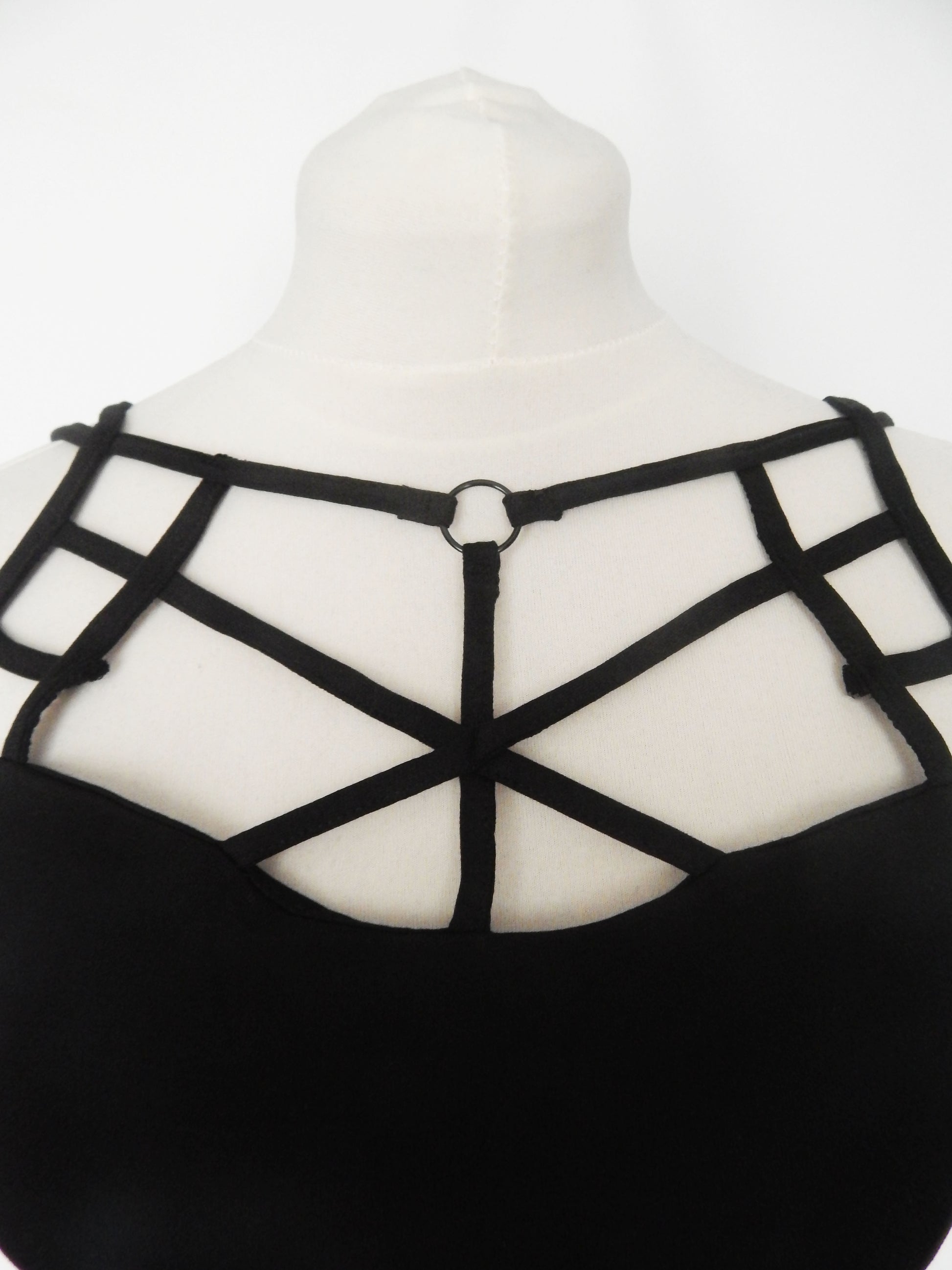 Black strappy crop top displayed on a white mannequin torso, showing a geometric crisscross strap design with a central ring detail.