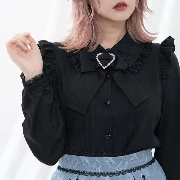 Close-up modelled photo of a black long sleeved blouse showing the Peter Pan style collar, ruffled shoulders, lace trimmed cuffs and detachable bow brooch. Styled with pink hair and a light blue lace skirt for a Jirai Kei aesthetic.