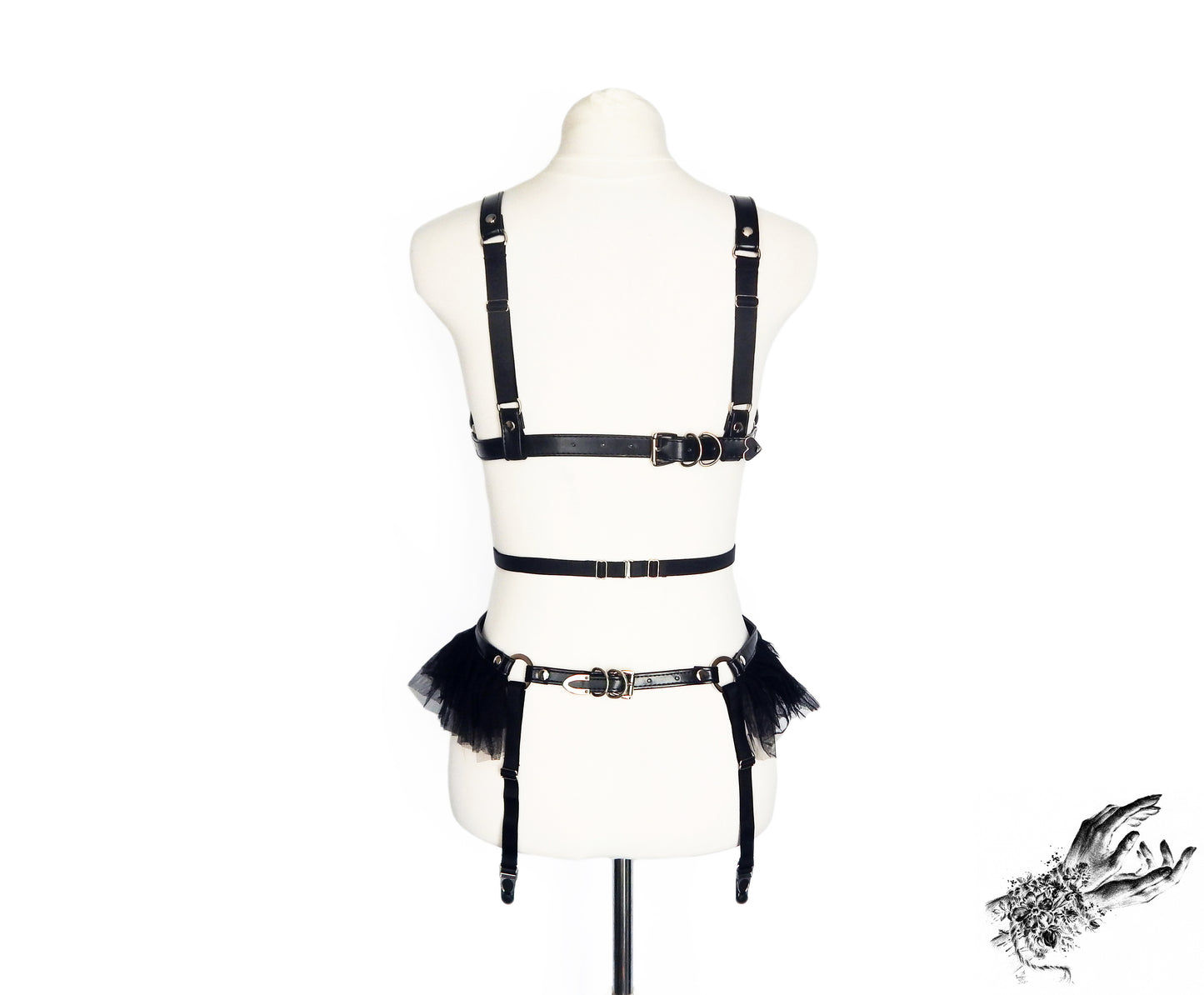 Rear view of a black vegan leather harness set showing the adjustable buckles and sliding elastic straps, displayed on a mannequin against a white background.