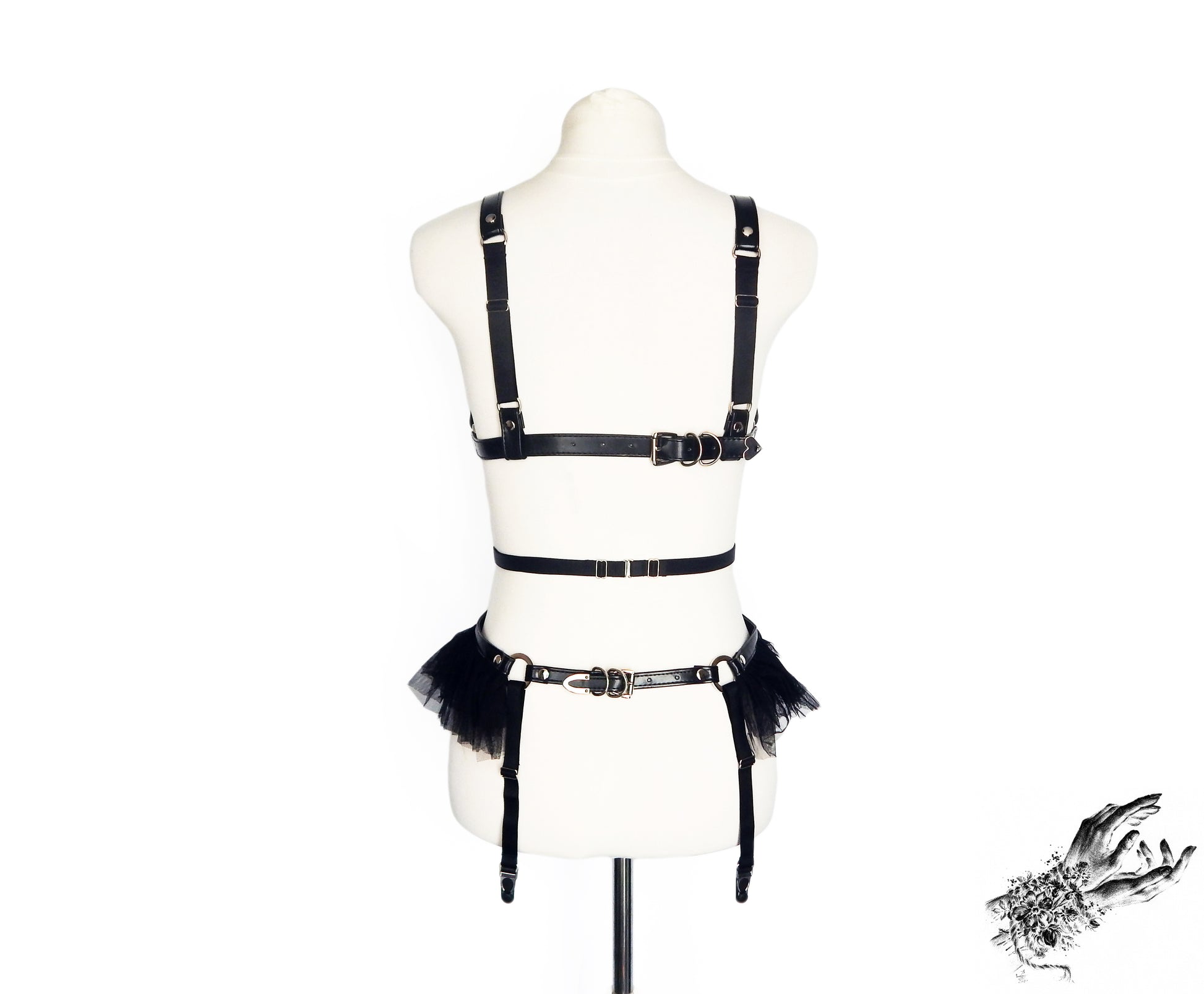 Rear view of a black vegan leather harness set showing the adjustable buckles and sliding elastic straps, displayed on a mannequin against a white background.