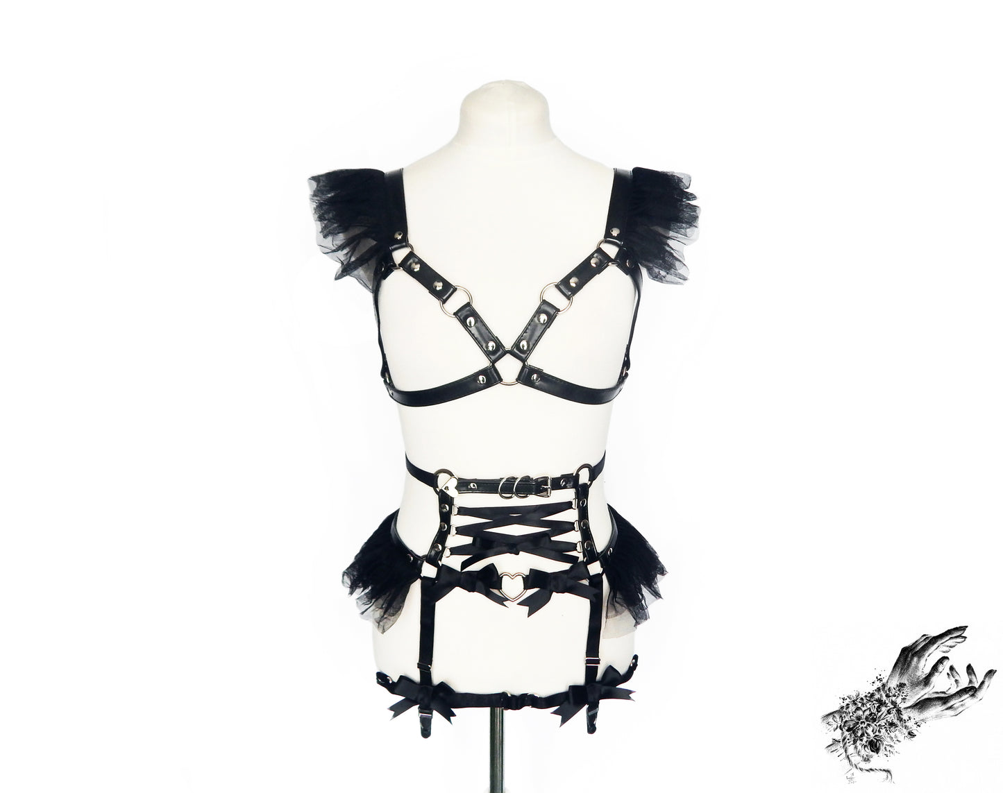 Black vegan leather harness set featuring a separate harness bra and garter belt with ruffled tulle accents, corset lacing and silver heart ring hardware, displayed on a mannequin against a white background.