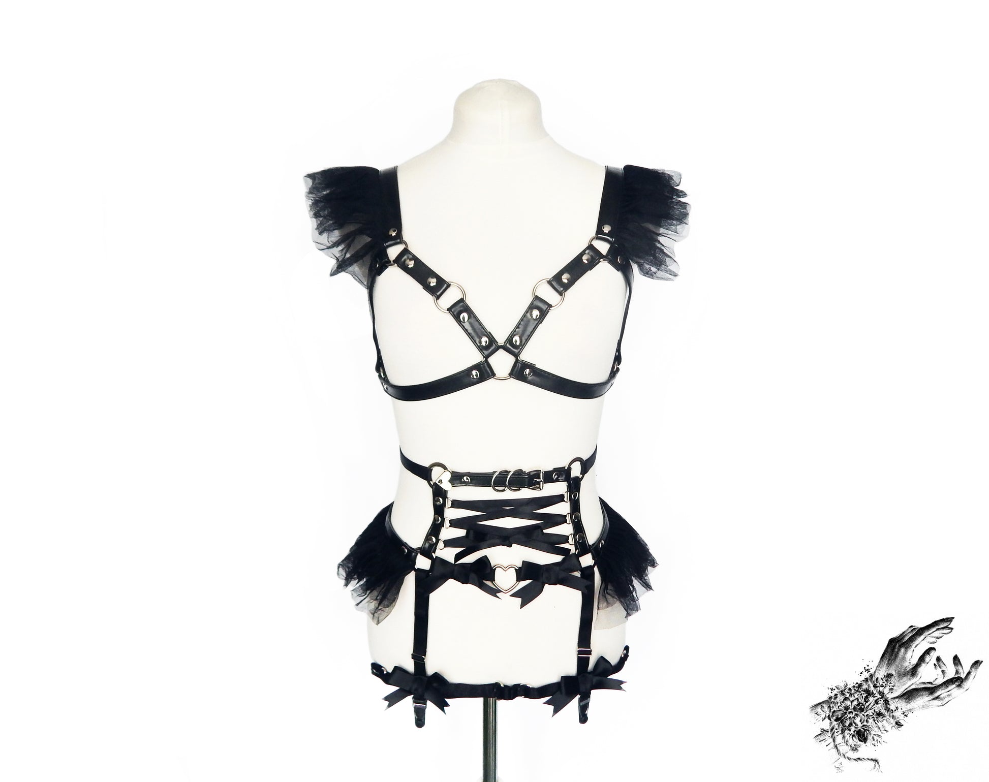 Black vegan leather harness set featuring a separate harness bra and garter belt with ruffled tulle accents, corset lacing and silver heart ring hardware, displayed on a mannequin against a white background.