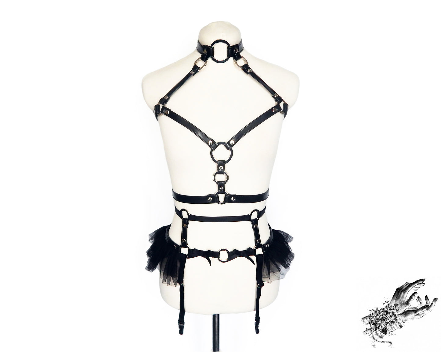 Front view of a black vegan leather harness set featuring silver O ring hardware, ruffled tulle and bow appliques, displayed on a mannequin against a white background.