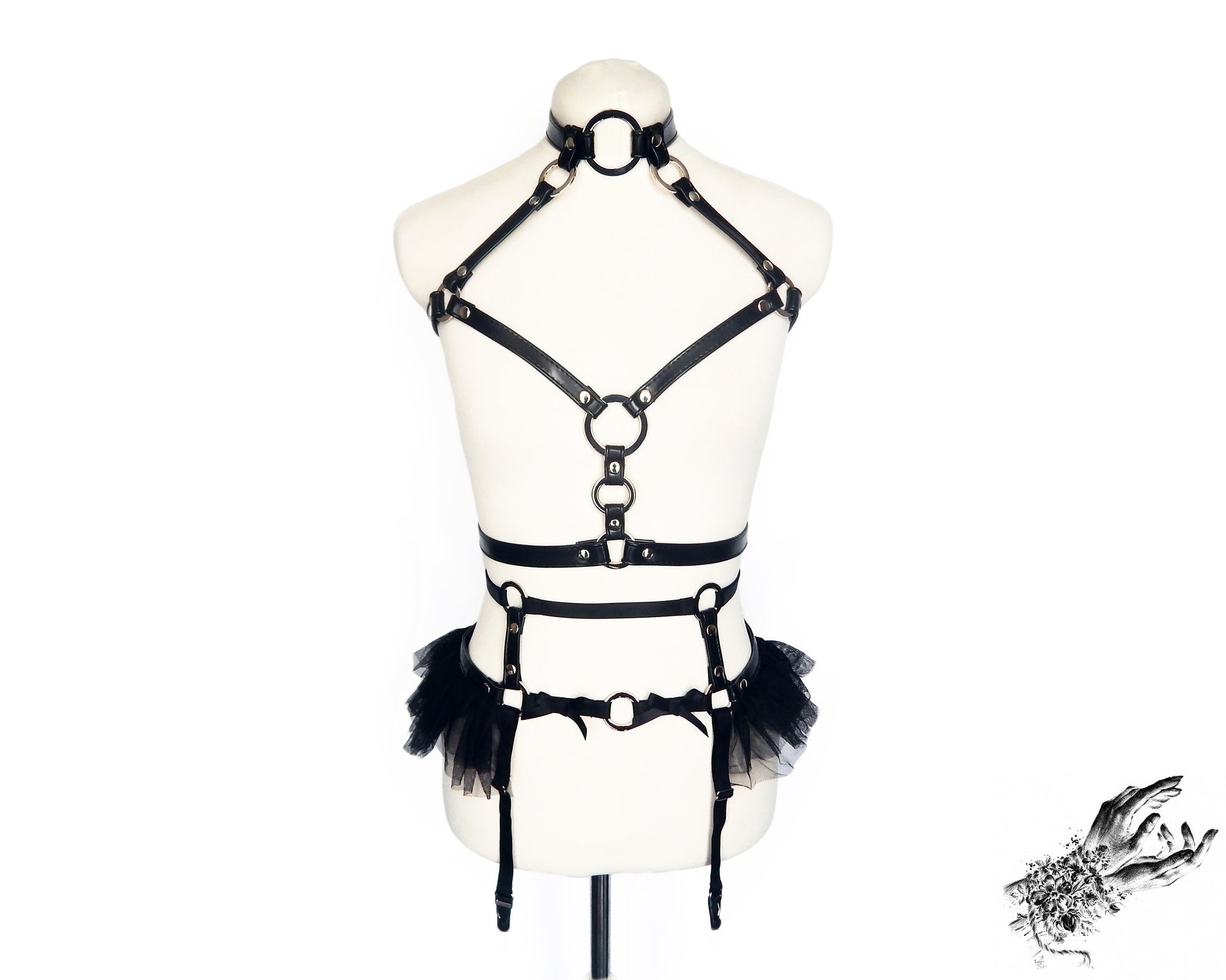 Front view of a black vegan leather harness set featuring silver O ring hardware, ruffled tulle and bow appliques, displayed on a mannequin against a white background.