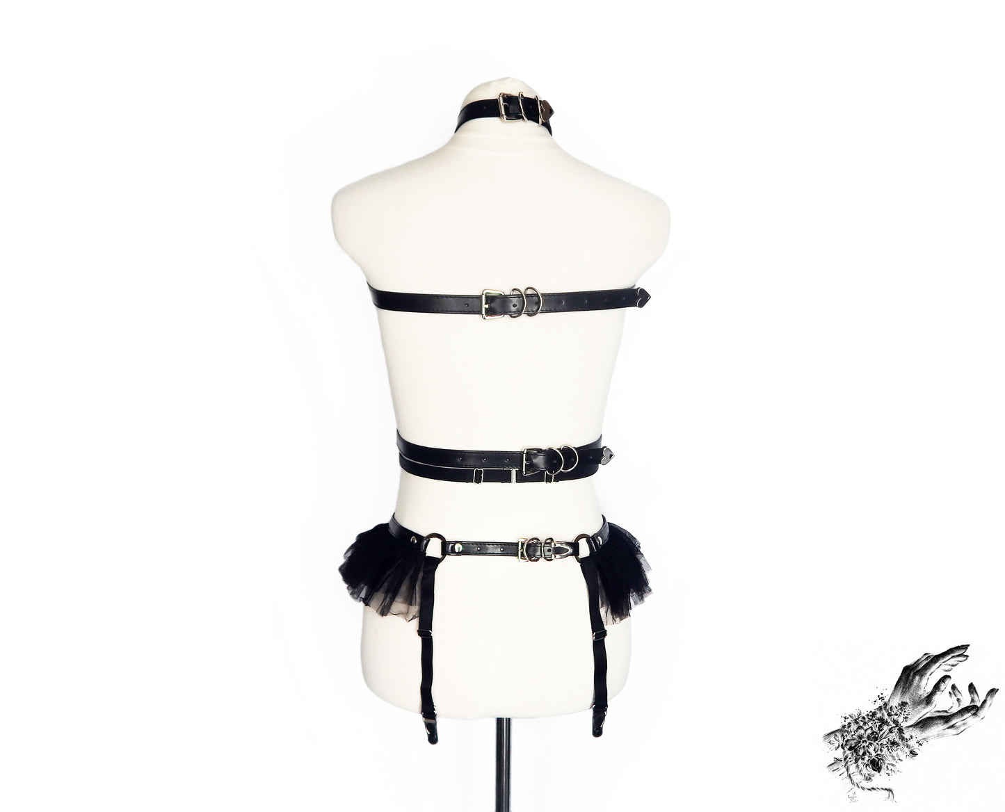 Rear view of a black vegan leather harness set showing adjustable buckled straps and sliding elastic straps, displayed on a mannequin against a white background.