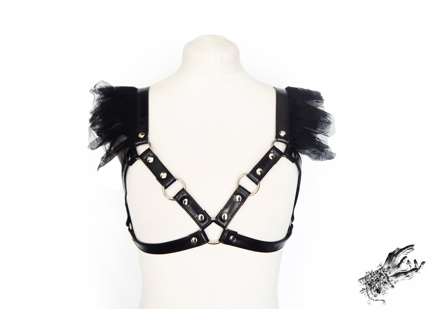 Black vegan leather harness bra featuring silver O ring hardware and ruffled tulle accents at the shoulders, displayed on a mannequin against a white background.