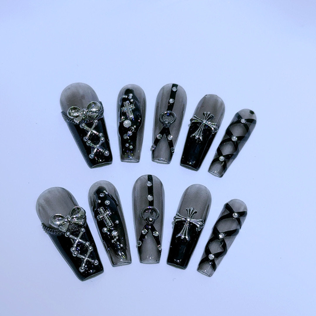 black and silver false nails displayed on a grey background, featuring 3D silver bows, crosses, O rings, clear diamantes and black bondages straps for a gothic fashion aesthetic.