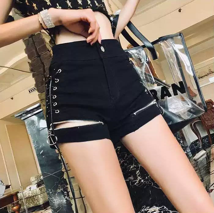black wide leg denim shorts featuring lace-up sides, zippered cuffs with O ring hardware, front zipper and button fastening with back pockets. styled with a black crop top for an alternative fashion aesthetic.