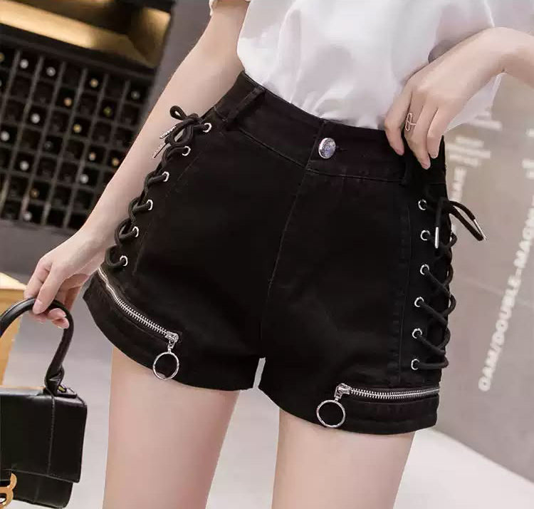 black wide leg denim shorts featuring lace-up sides, zippered cuffs with O ring hardware, front zipper and button fastening with back pockets. styled with a white tucked in blouse and black handbag for a casual fashion aesthetic.