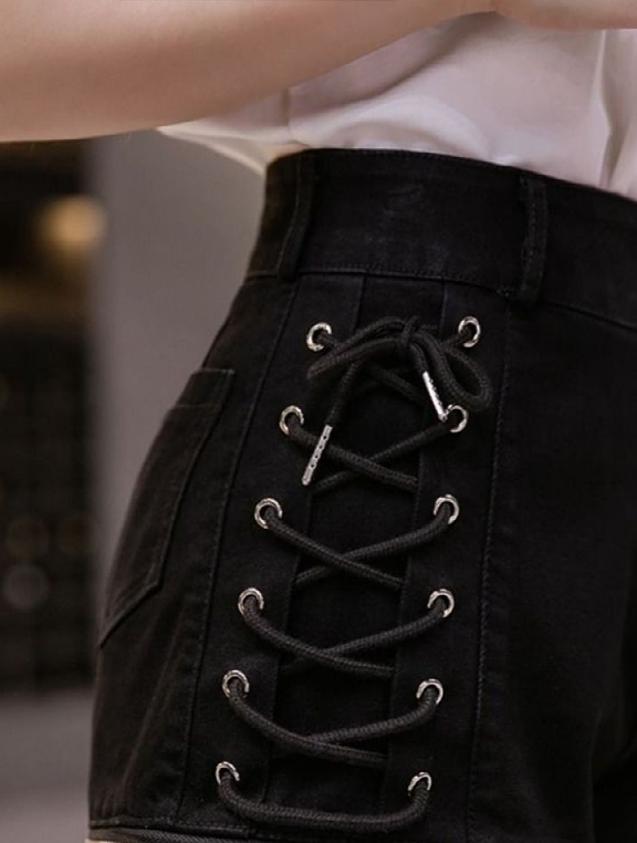 Close-up of black high-waisted shorts with a lace-up side panel and silver metal eyelets, worn with a white top.