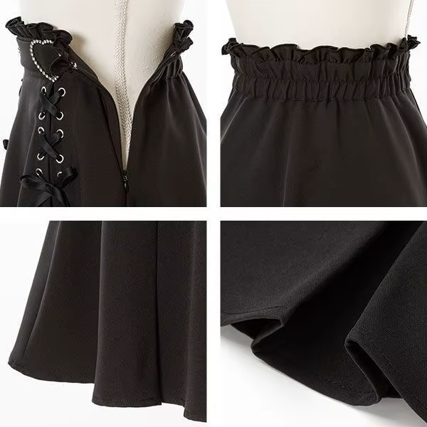 Detail photo of a black high waisted skirt featuring a partially elasticated waist with side zip fastening, diamante heart shaped buckle belt, satin ribbon corset lacing and pleated a-line design, displayed on a mannequin against a white background.