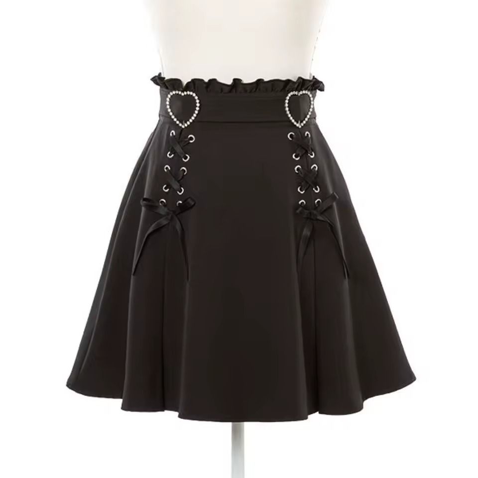 Black high waisted skirt featuring a ruffled waist, diamante heart shaped buckle belt, satin ribbon corset lacing and pleated a-line design, displayed on a mannequin against a white background.