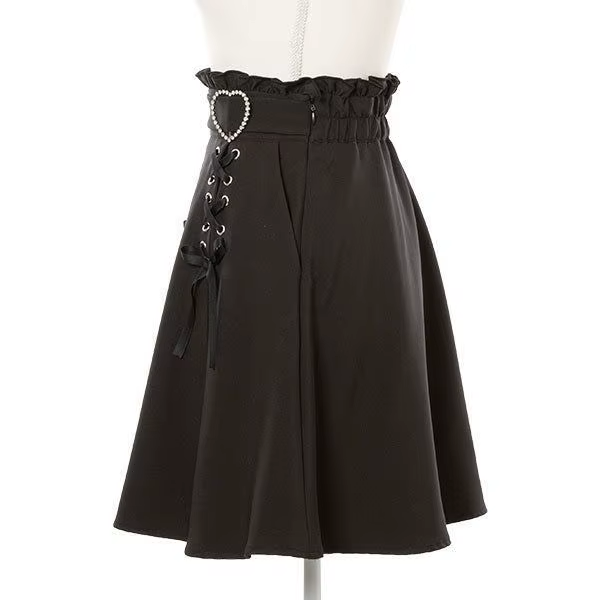 Side view of a black high waisted skirt featuring a ruffled waist with side zip fastening, diamante heart shaped buckle belt, satin ribbon corset lacing and pleated a-line design, displayed on a mannequin against a white background.