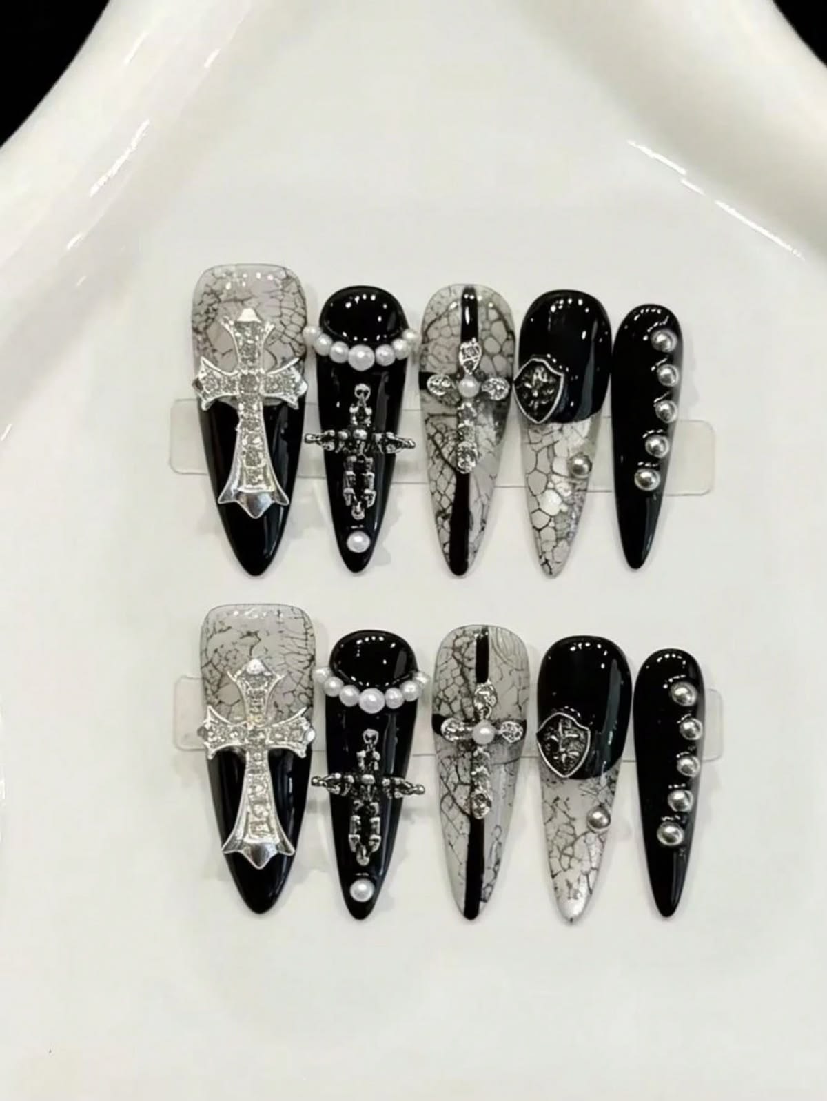 Black and white long stiletto false nails featuring a gothic snakeskin pattern, silver metal crosses and shields, white pearl beads and miniature studs, displayed on a white background.