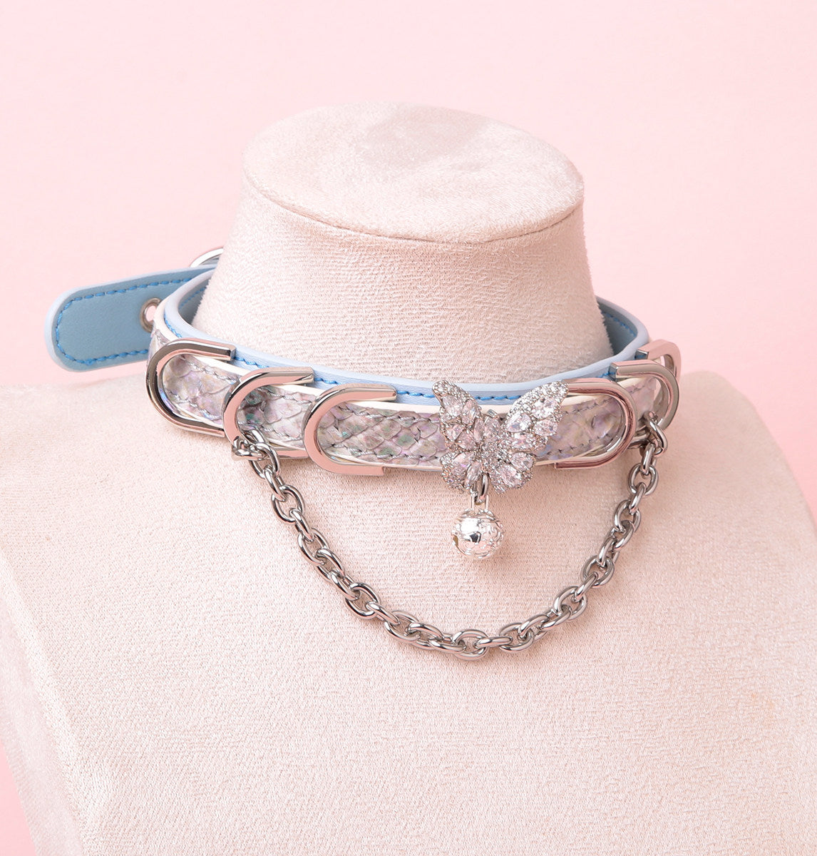 Blue and iridescent silver leather choker featuring a silver diamante butterfly charm, chains, D rings and bell. Displayed on a white mannequin bust against a pink background for a kawaii fashion aesthetic.