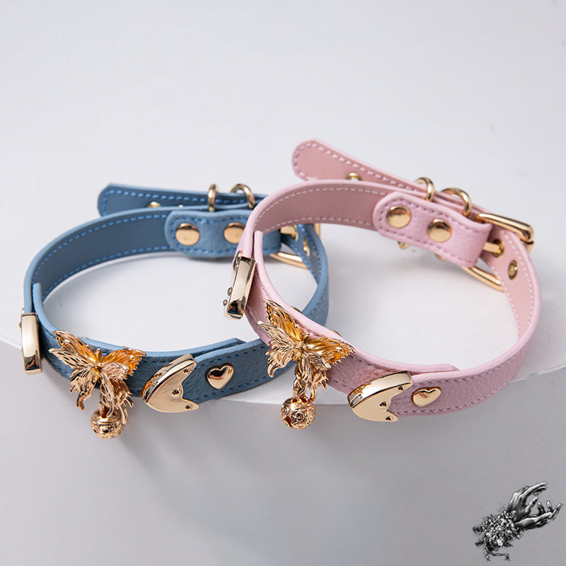 Two blue and pink leather chokers next to each other, featuring ornate gol butterfly and bell hardware for a pastel goth and kawaii fashion style