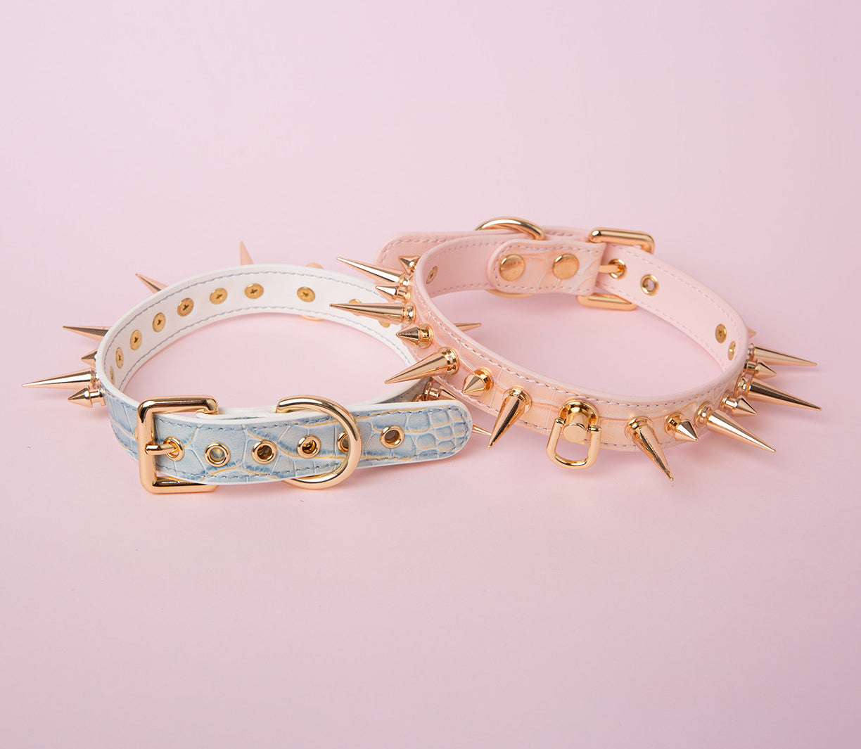 Rear view of two pink and blue faux crocodile effect leather chokers showing the gold tone adjustable buckle and multiple sizing holes for a versatile fit. Displayed on a pink background for a Harajuku fashion aesthetic.
