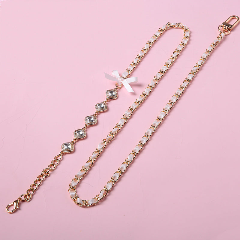 Close-up of a pink and gold chain leash for the Cleo choker design, featuring intricate pink satin ribbon threaded through gold curb chain, gold and clear crystal charms and swivel lobster clasps. Displayed on a pink background for a pet play aesthetic.