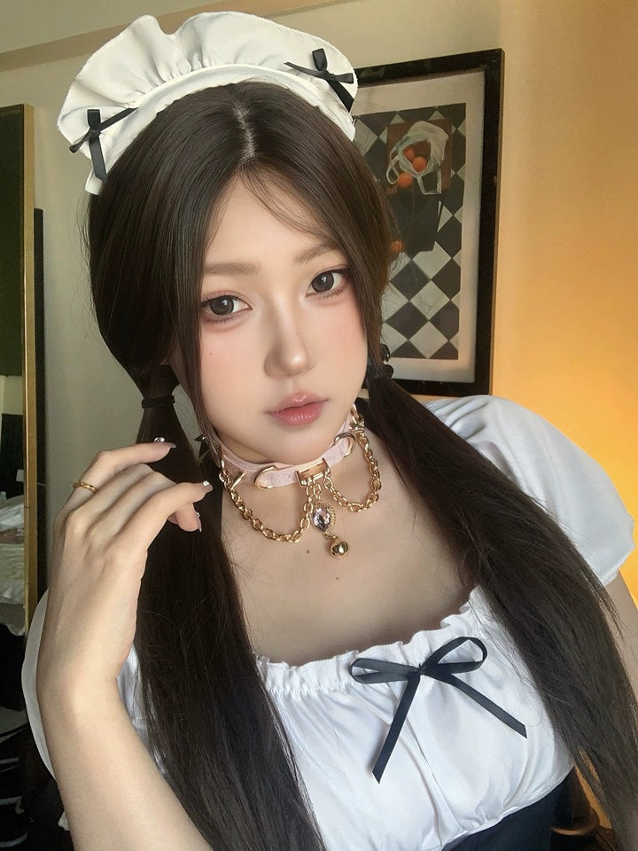 Worn photo of a pink leather choker featuring gold tone chains, D rings, spike studs, bell and pink and gold crystal heart charm. Styled with a black and white maid costume for a kawaii idol aesthetic.