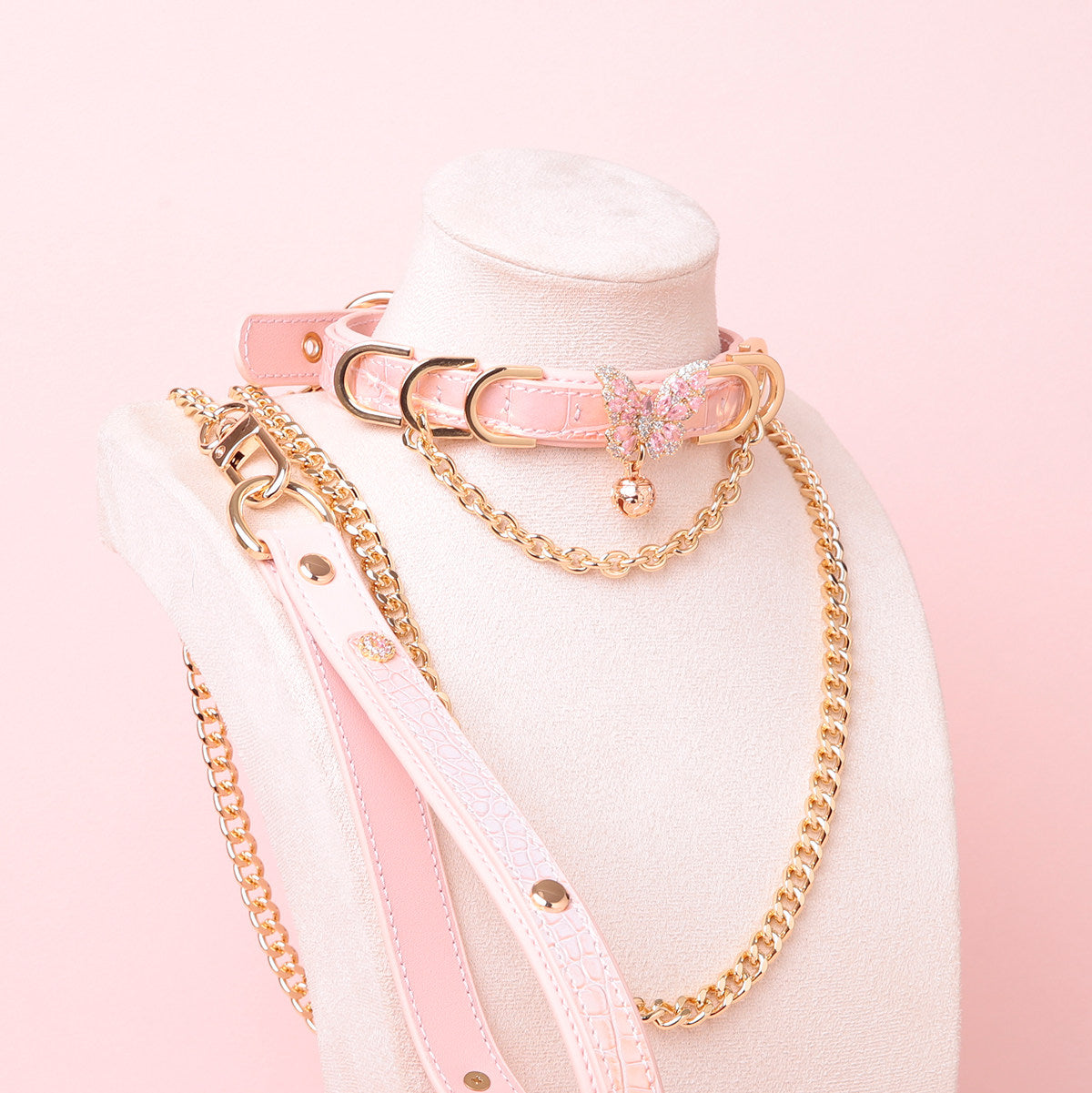 Pink leather choker and leash set featuring a gold and pink diamante butterfly charm, chains, D rings and bell, with detachable chain leash and leather hand strap. Displayed on a white mannequin bust against a pink background for a Harajuku fashion aesthetic.