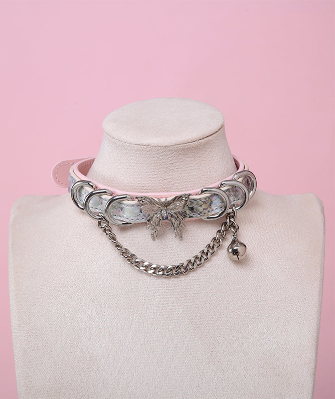 Pink and holographic silver leather choker featuring a stainless steel plated butterfly charm, D rings, chain and bell. Displayed on a white mannequin bust against a pink background for a pastel goth aesthetic.