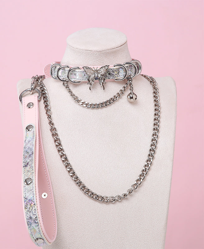 Pink and holographic silver leather choker and leash set featuring stainless steel plated butterfly hardware, D rings, chain and bell with detachable chain leash and leather hand strap. Displayed on a white mannequin bust against a pink background for a Cybergoth aesthetic.