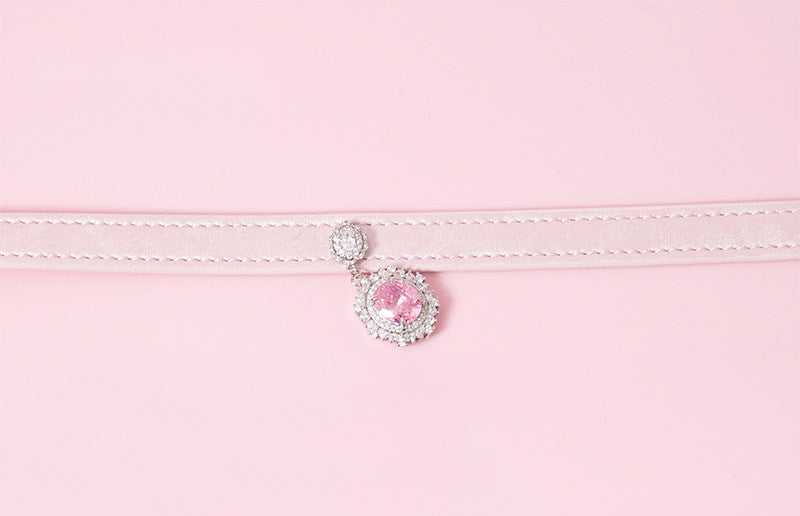 Close-up of a pink leather choker showing the silver and pink crystal cameo and hardware. Displayed on a pink background for a kawaii fashion aesthetic.