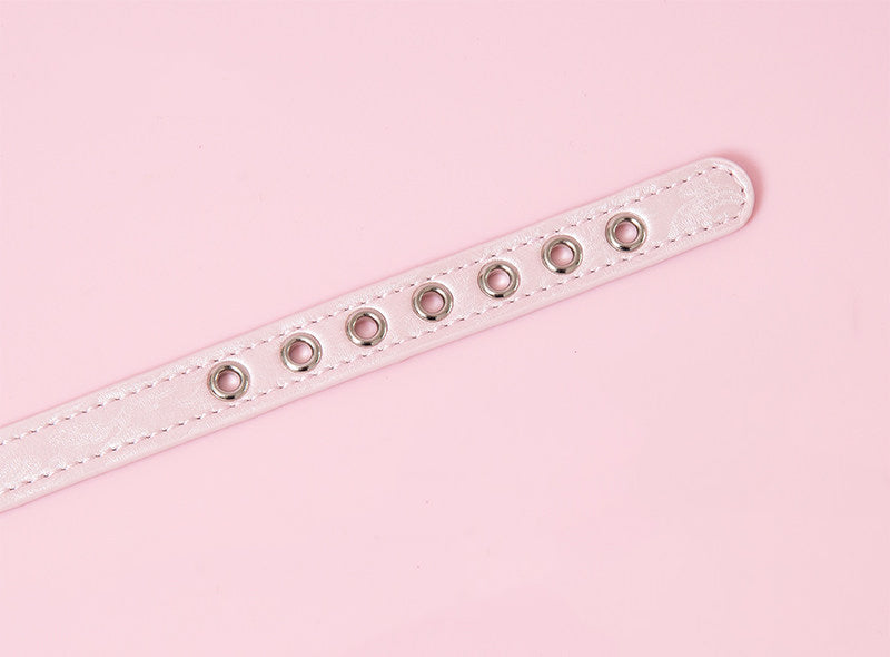 Close-up of a pink leather choker showing multiple stainless steel plated eyelet holes, ensuring a durable and versatile fit. Displayed on a pink background for a kawaii fashion aesthetic.