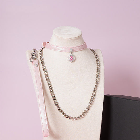 Pink leather choker and leash set featuring clear and pink crystal cameo and hardware, detachable silver chain leash and pink leather hand strap. Displayed on a white mannequin bust against a pink background for a pastel goth aesthetic.
