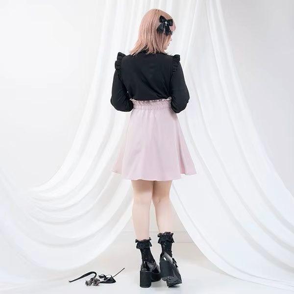 Modelled photo of the back of a pink high waisted skirt featuring a partially elasticated waist, side zip fastening and pleated a-line design, styled with a black blouse and chunky black Mary Jane shoes for a Jirai Kei fashion aesthetic.