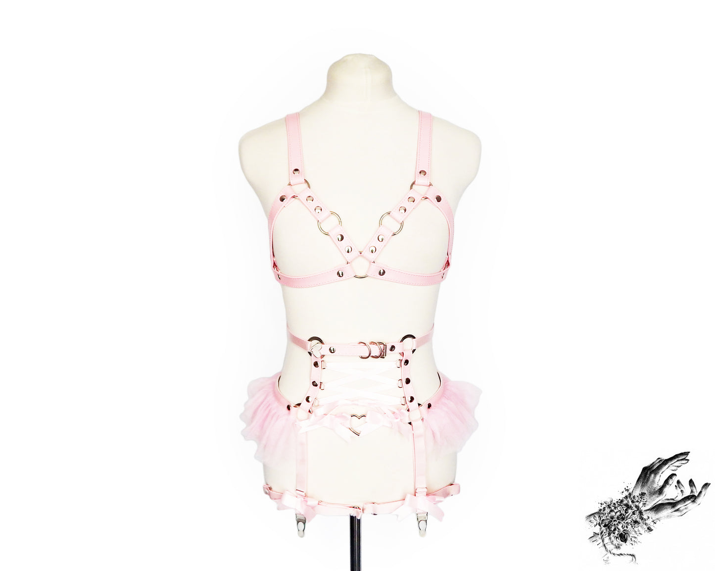 Pink vegan leather harness set featuring silver O ring hardware, pink ruffled tulle accents at the waist and corset lacing, displayed on a mannequin against a white background.
