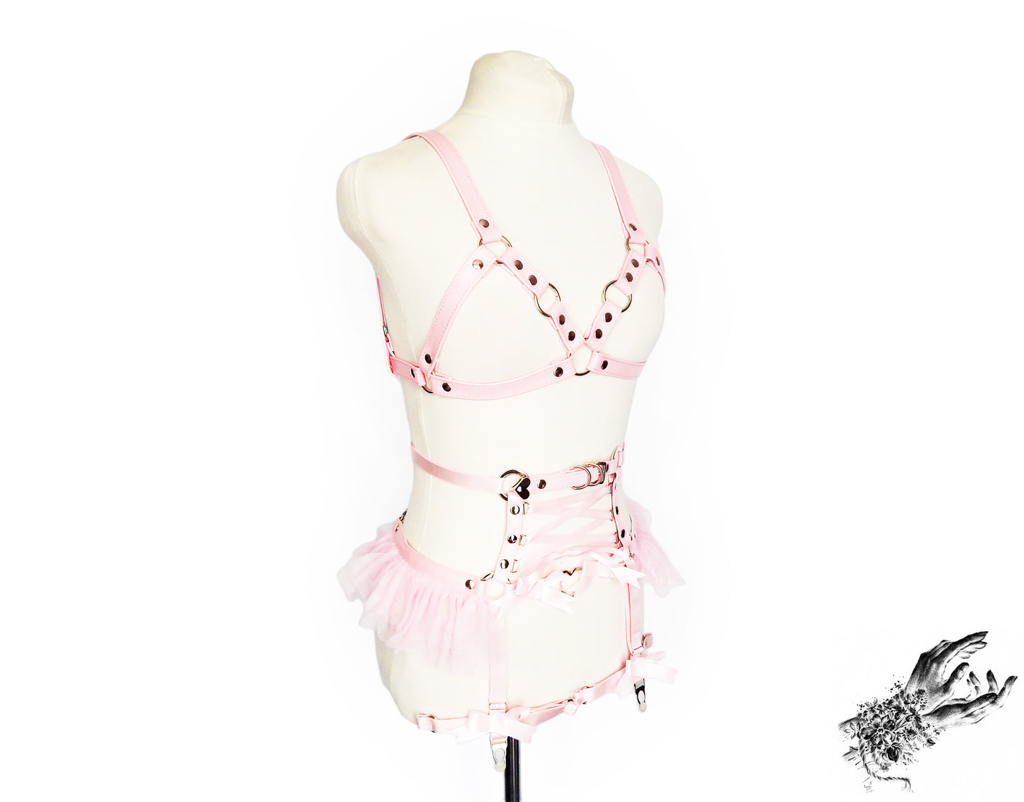 Side view of a pink vegan leather harness set featuring silver O ring hardware, pink ruffled tulle accents at the waist and corset lacing, displayed on a mannequin against a white background.