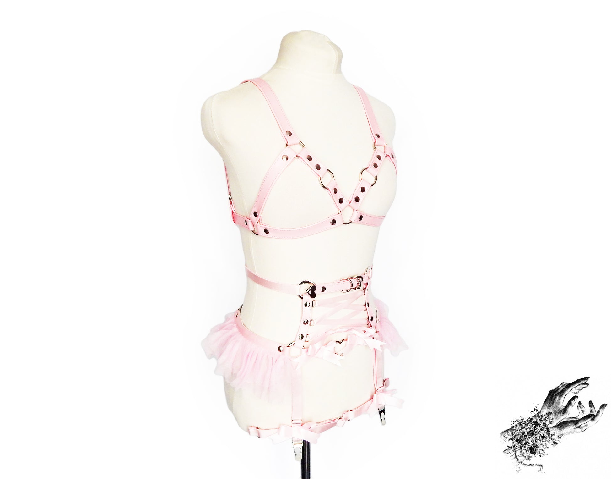 Side view of a pink vegan leather harness set featuring silver O ring hardware, pink ruffled tulle accents at the waist and corset lacing, displayed on a mannequin against a white background.