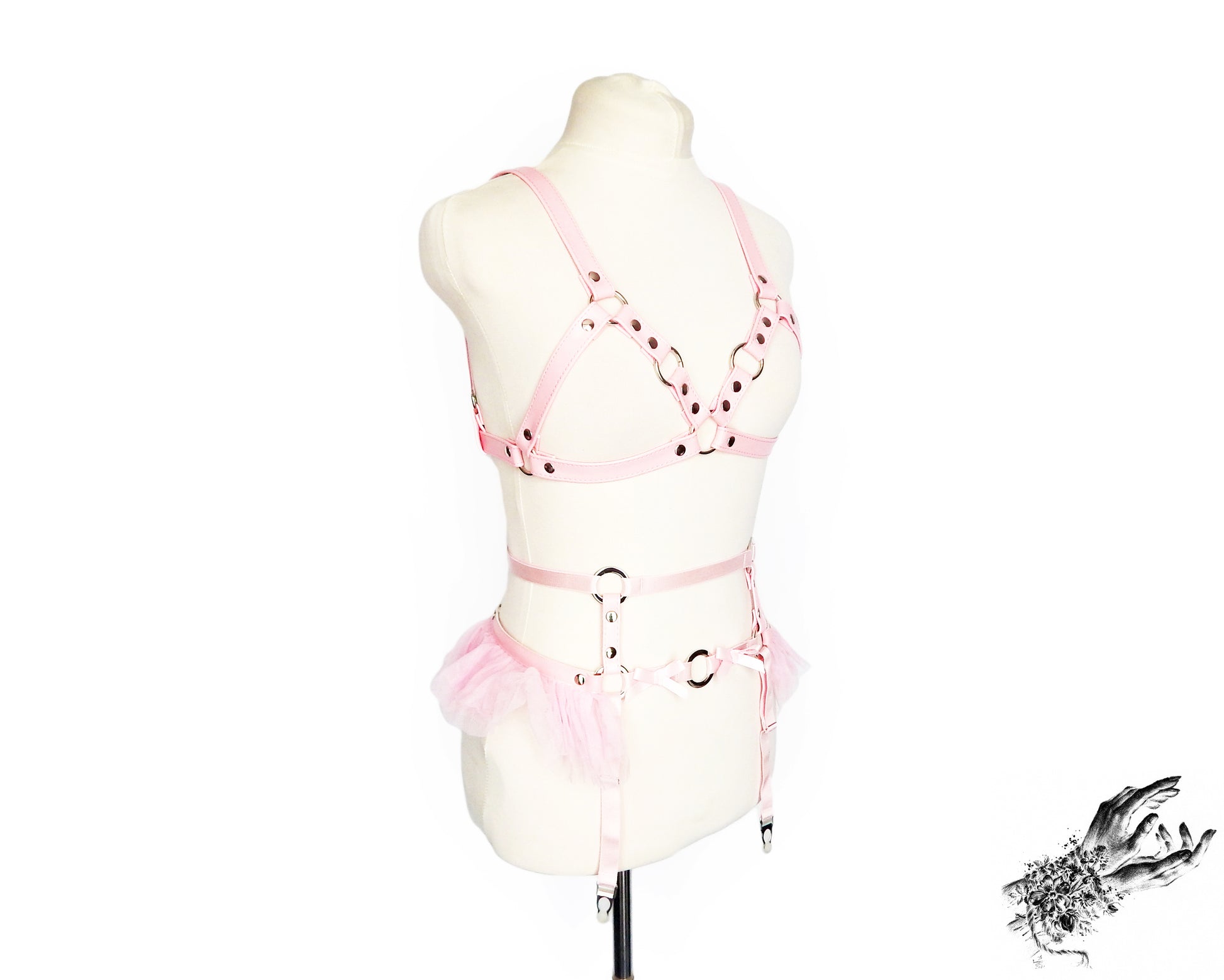 Side view of a pink faux leather harness set featuring a separate harness bra and garter belt with silver O ring hardware, pink ruffled tulle and bow appliques, displayed on a mannequin against a white background.