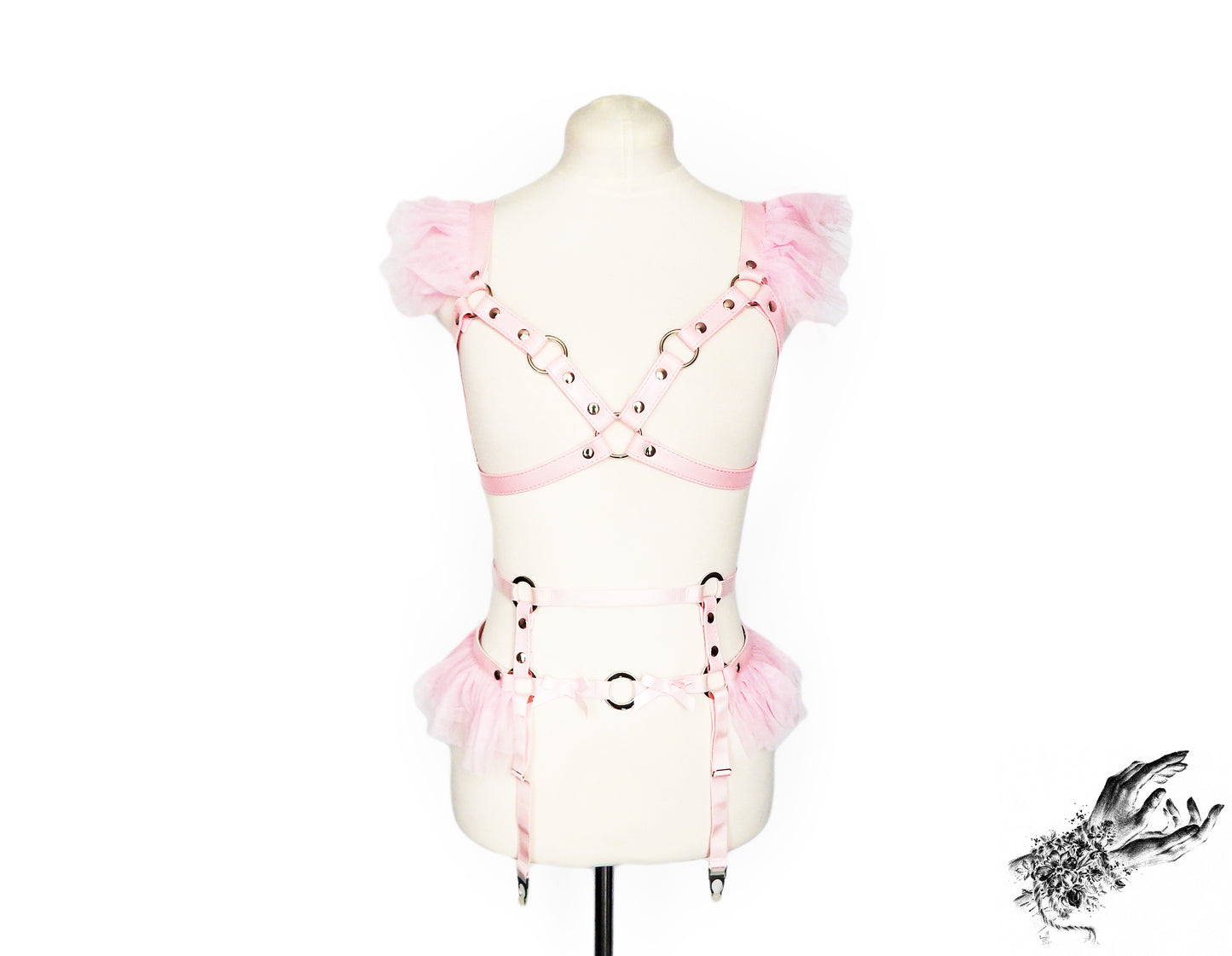 A light pink vegan leather harness set with ruffled tulle shoulder and waist details, displayed on a cream-colored mannequin torso against a white background.