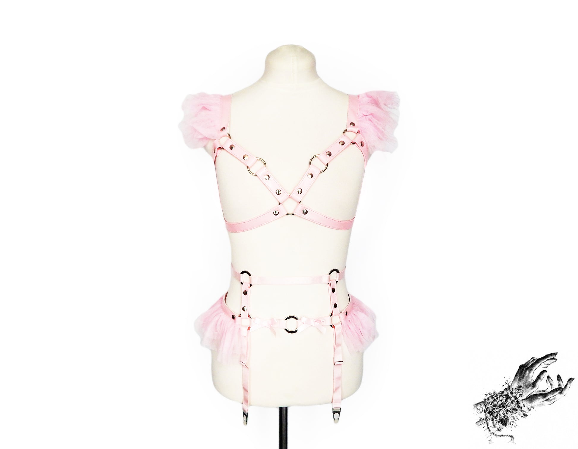 A light pink vegan leather harness set with ruffled tulle shoulder and waist details, displayed on a cream-colored mannequin torso against a white background.