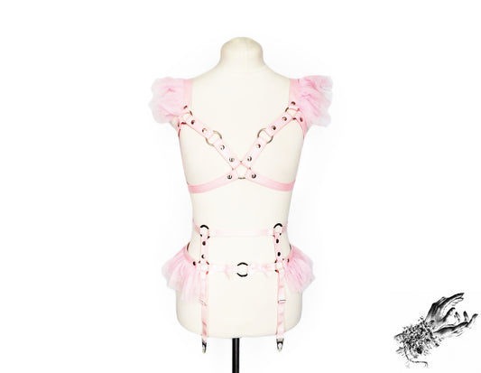 A light pink vegan leather harness set with ruffled tulle shoulder and waist details, displayed on a cream-colored mannequin torso against a white background.
