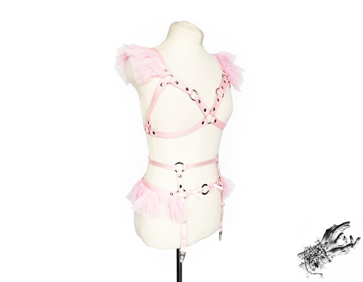 A pink vegan leather harness set with matching pink ruffled tulle at the shoulders and waist and silver O ring hardware. Displayed on a cream mannequin against a white background.