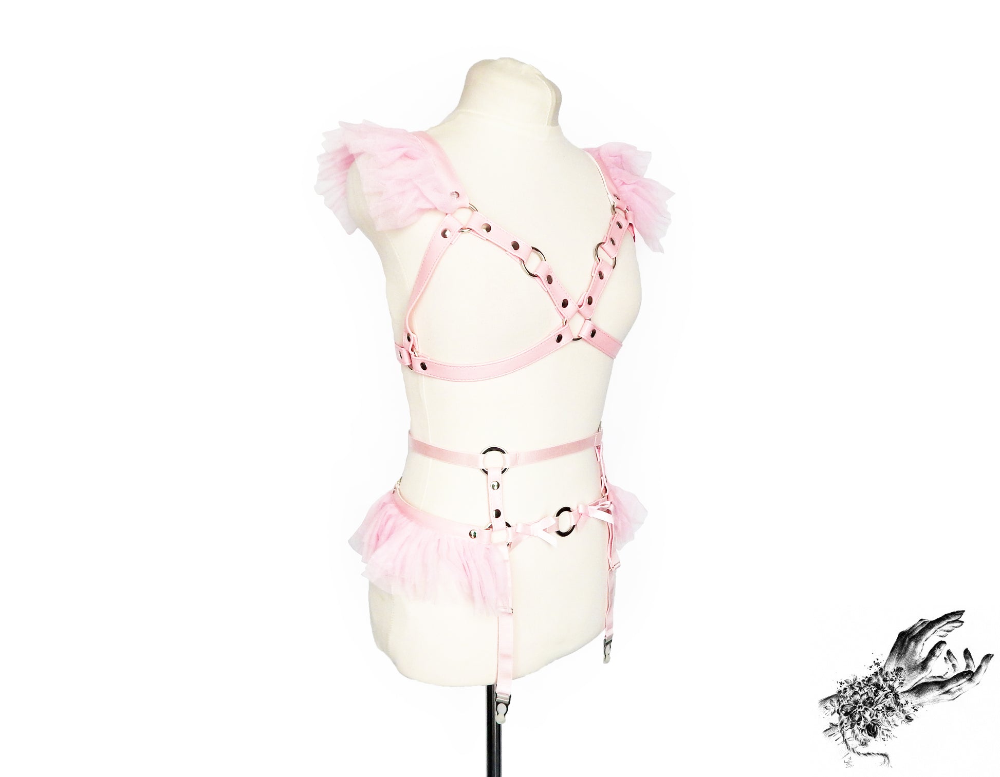 A pink vegan leather harness set with matching pink ruffled tulle at the shoulders and waist and silver O ring hardware. Displayed on a cream mannequin against a white background.